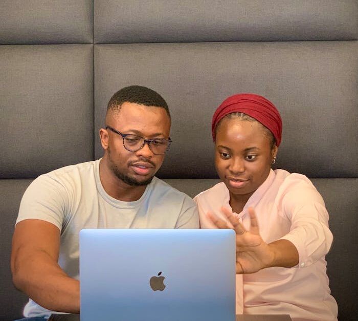 Two people collaborating on a laptop indoors with a modern wall backdrop.